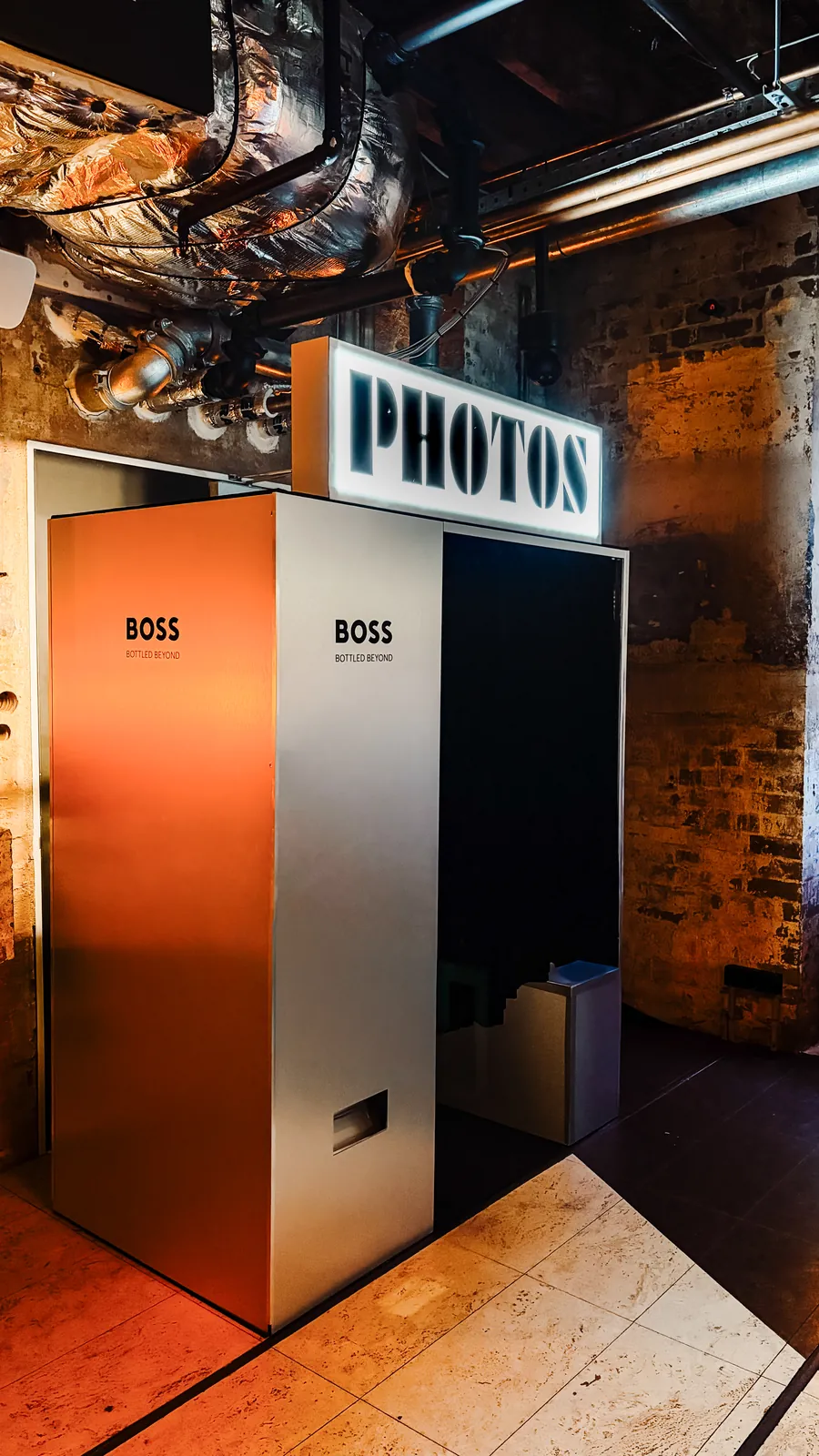 Booth with an orange BOSS-branded panel under a lit PHOTOS sign